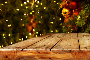 Christmas and New year background with empty dark wooden deck table over christmas tree and blurred light bokeh. Empty display for product montage. Rustic vintage Xmas background.