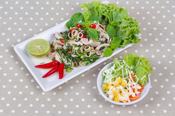 Spicy and sour mixed herb salad with pork and chicken served with side dish on gray.  Side view