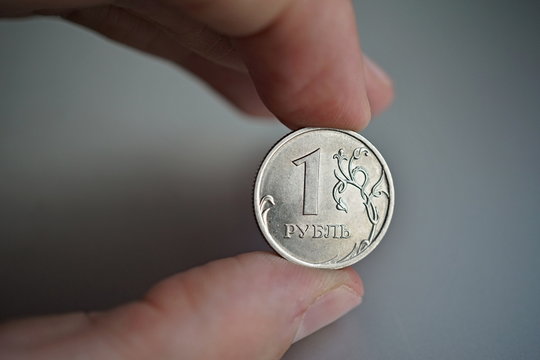 
Male hand holding a shiny silver coin of one Ruble (Rouble) as a symbol of Russian currency  