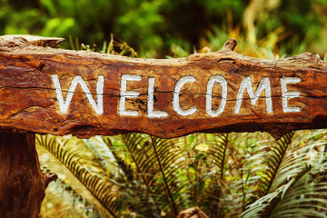 Wooden placard with greeting caption Welcome at tropical park