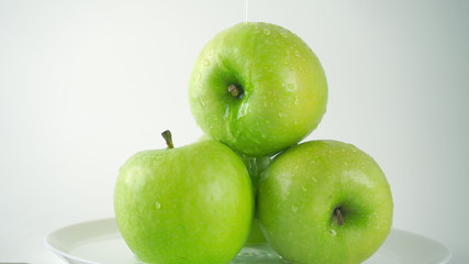 Water being poured over green apples, light gray background