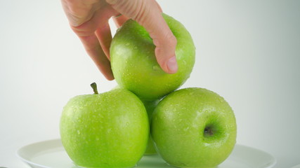 Girl's hand taking one wet green apple, light background