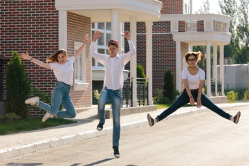 Three joyful teenagers friends having fun together on the street jumping up in the air, sunny outdoors