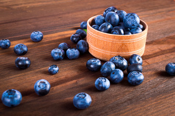 Blueberry berries in a wooden glass scattered on the wooden table.