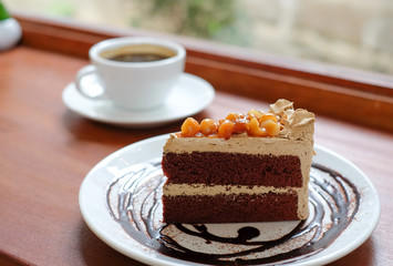 Macadamia chocolate cake with white coffee cup on wooden floor.