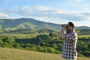 Man is using binoculars to explore wonderful summer scenic landscape in mountain