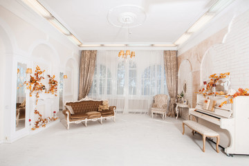 Great white hall in majestic classical style with columns, arches, mirrors, vintage furniture, piano. Decorated in autumn colors. Wide angle.