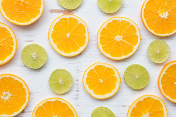 Orange slices and green lemon on white rustic wooden background, top view, flat lay, summer and healthy concept