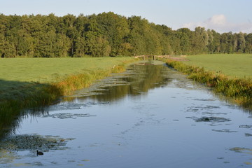 River with a bridge spanning across it, flanked by fields of grass