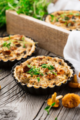 Homemade tarts of puff pastry with seasonal chanterelle mushrooms, cheese, thyme and onion on rustic wooden table, selective focus