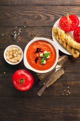 Homemade tomato soup with tomatoes, red pepper, herbs and spices on dark rustic wooden background, top view
