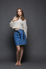 Portrait of beauty young woman in white fashion female pullover and blue jeans skirt on gray background