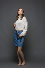 Portrait of beauty young woman in white fashion female pullover and blue jeans skirt on gray background