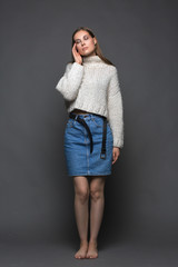 Portrait of beauty young woman in white fashion female pullover and blue jeans skirt on gray background
