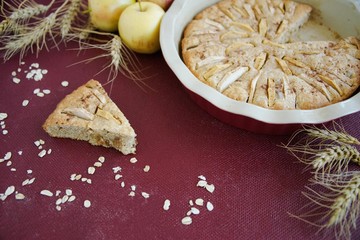 Homemade apple pie in the baking dish with apples and ears of wheat on the burgundy background