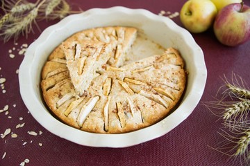 Homemade apple pie in the baking dish with apples and ears of wheat on the burgundy background
