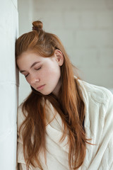 Closeup portrait of young adorable redhead woman wrapped in a white knitted blanket posing near white wall indoor natural light