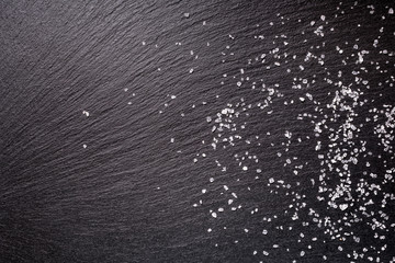 sprinkled sea salt over black slate stone background, top view