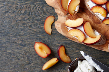Italian appetizer bruschetta with fresh plums and cream cheese on dark wooden background