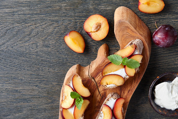 Italian appetizer bruschetta with fresh plums, cream cheese and mint leaves on dark wooden background