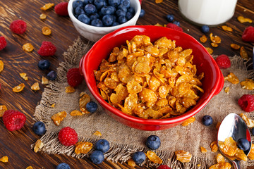 Corn Flakes with berries raspberries, blueberries, glass of milk, and sweet honey.