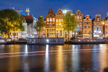 Amsterdam canal Amstel with typical dutch houses, houseboat and luminous track from the boat at night, Holland, Netherlands.