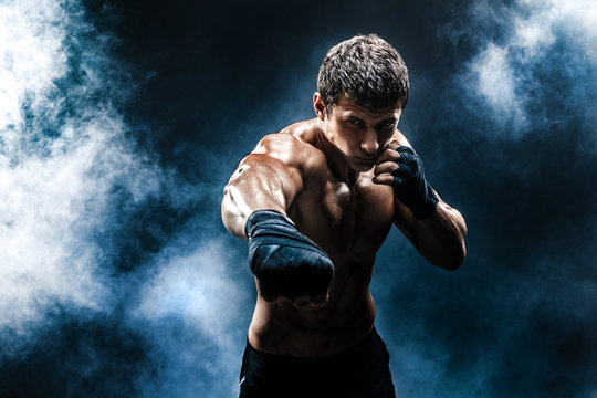 Muscular kickbox or muay thai fighter punching in smoke.