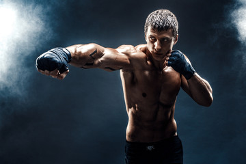Muscular kick-box or muay thai fighter punching in smoke.