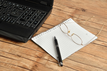 A laptop with reading glasses, a pen and a note book