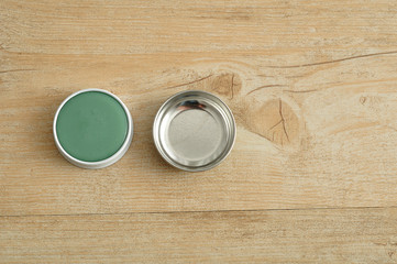 A green ointment in a white tin with a silver lid 