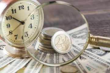 Time is money finance concept with old vintage clocks, dollar bills, magnifying glass and euro coins