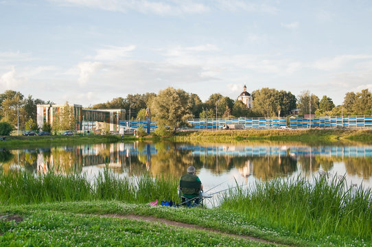 Large pond of Long ponds in the North of Moscow. A fisherman catches a fish. Summer evening landscape