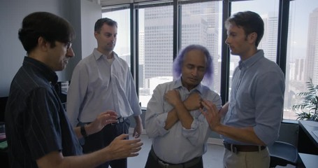 Group of four business men led by creative executive with purple hair take part in a trust building exercise with leader being caught by others.  Wide shot, recorded hand held in slow motion at 60fps