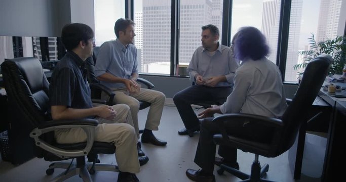 Group of four business men led by creative executive with purple hair throw bean bag to each other in team building exercise in Downtown LA office.  Wide shot, recorded in slow motion at 60fps