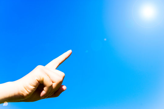 Female pointing finger under blue sky, with lens flare