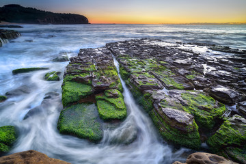 The wave flows over weathered rocks and boulders at Turimetta Be