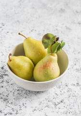 Fresh organic pears in a white bowl on a light background