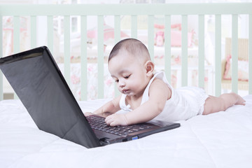 Curious toddler playing laptop on bed