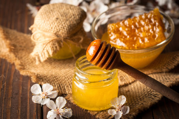 Honey dripping from a wooden honey dipper in a jar on wooden grey rustic background. Propolis and bee honey. Spring natural product concept.