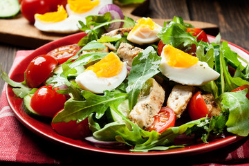 Fresh salad with chicken, tomatoes, eggs and arugula on plate
