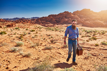 bearded man carrying stuicase through the desert in nevada