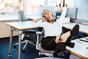 Young beautiful successful businesswoman resting, relaxing at workplace, over office background.