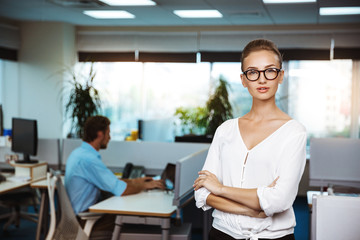 Fototapeta premium Young successful businesswoman smiling, posing with crossed arms, over office background.