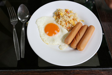 Fried rice with fried egg and sausage on white dish.