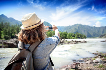 Young woman traveler on a background of mountains takes photos o