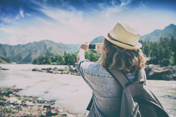 Young woman traveler on a background of mountains takes photos o