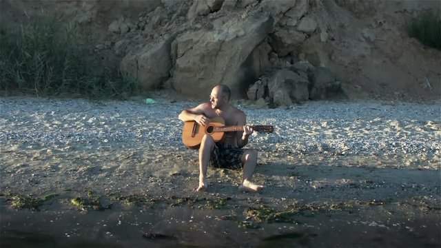 The guy playing the guitar at sunset on the beach. Slowmotion