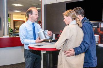 Salesman Showing Compact Speaker To Couple In Shop