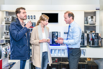 Obraz premium Salesman Showing Espresso Cups To Couple In Electronic Shop