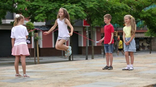 Smiling kids in school age playing together with jumping rope outdoors